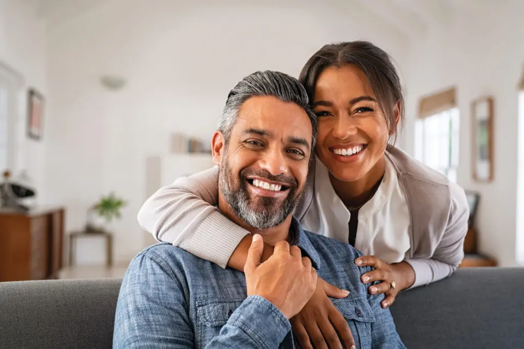 A woman wraps her arm around her husband, the happy couple smiles